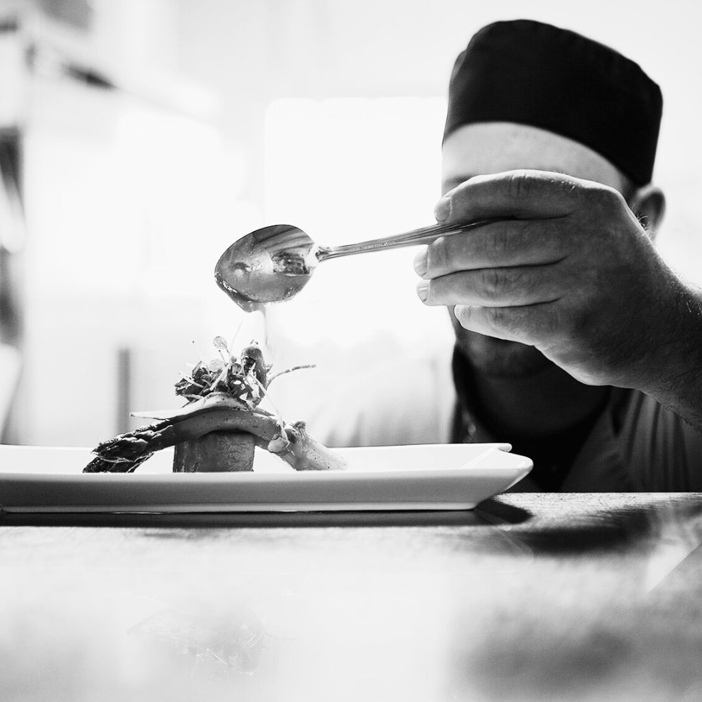 Chef voegt de finishing touch toe aan een gerecht onder hoge werkdruk in de horeca.